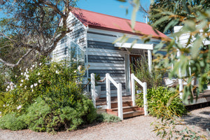 Small grey and white cabin with a red roof surrounded by greenery