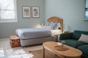 Bedroom with a queen bed, green sofa, wooden coffee table, and framed artwork on the wall.